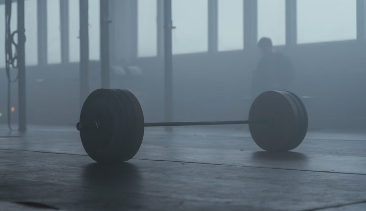 A lone barbell on the gym floor with a misty background creates a mysterious and moody ambiance.