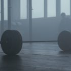 A lone barbell on the gym floor with a misty background creates a mysterious and moody ambiance.