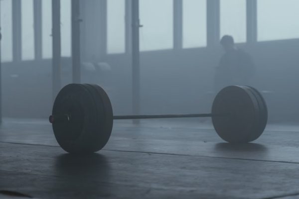 A lone barbell on the gym floor with a misty background creates a mysterious and moody ambiance.